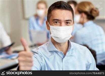 business, people and pandemic concept - businessman wearing face protective medical mask for protection from virus disease showing thumbs up at office. businessman in mask showing thumbs up at office