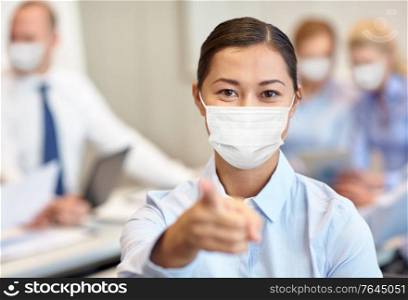 business, people and pandemic concept - businesswoman wearing face protective medical mask for protection from virus disease pointing finger to camera at office. businesswoman in mask pointing finger at office