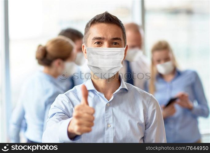 business, people and pandemic concept - middle aged businessman wearing face protective medical mask for protection from virus disease showing thumbs up at office. businessman in mask showing thumbs up at office