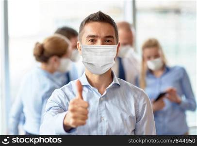 business, people and pandemic concept - middle aged businessman wearing face protective medical mask for protection from virus disease showing thumbs up at office. businessman in mask showing thumbs up at office