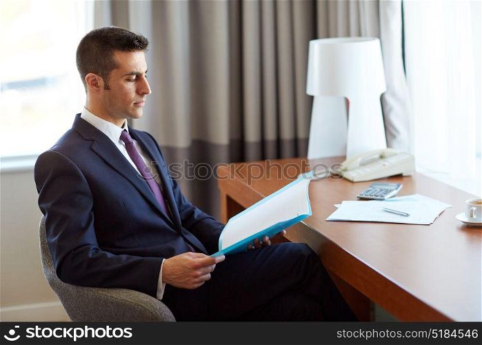 business, people and paperwork concept - businessman with papers in folder working at hotel room. businessman with papers working at hotel room