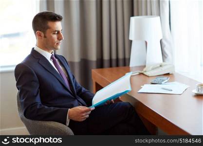 business, people and paperwork concept - businessman with papers in folder working at hotel room. businessman with papers working at hotel room