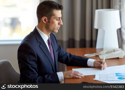 business, people and paperwork concept - businessman with papers working at hotel room. businessman with papers working at hotel room