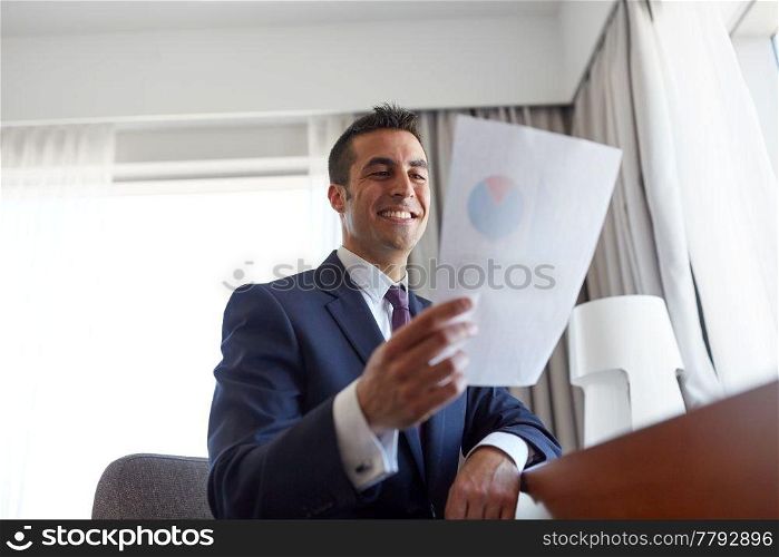 business, people and paperwork concept - businessman with papers working at hotel room. businessman with papers working at hotel room