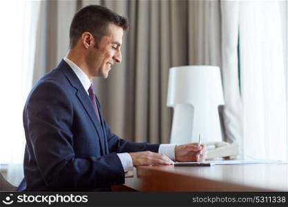 business, people and paperwork concept - businessman working and signing papers at hotel room. businessman with papers working at hotel room