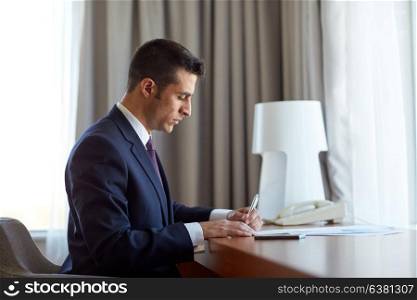 business, people and paperwork concept - businessman working and signing papers at hotel room. businessman with papers working at hotel room