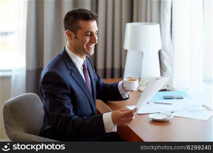 business, people and paperwork concept - happy smiling businessman with papers drinking coffee at hotel room. businessman with papers drinking coffee at hotel
