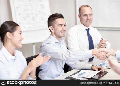 business, people and partnership concept - smiling business team shaking hands and applauding in office
