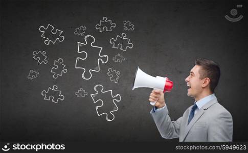 business, people and public announcement concept - happy businessman in suit speaking to megaphone and puzzle doodles over dark gray concrete wall background