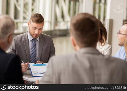 business, people and statistics concept - business team with graph on clipboard meeting at office