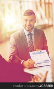 business, people and statistics concept - happy smiling young businessman with graph on clipboard meeting with colleague at office. smiling businessman with graph at business meeting
