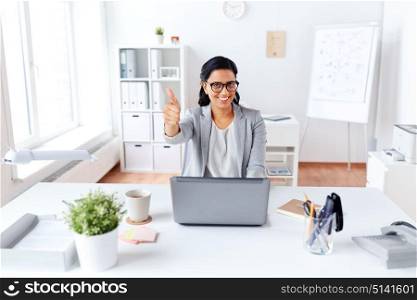 business, people and success concept - happy smiling businesswoman with laptop computer showing thumbs up at office. happy businesswoman showing thumbs up at office