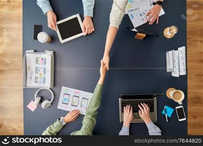 business, people and team work concept - team of startuppers with gadgets and papers makes handshake at office table. business team makes handshake at office table