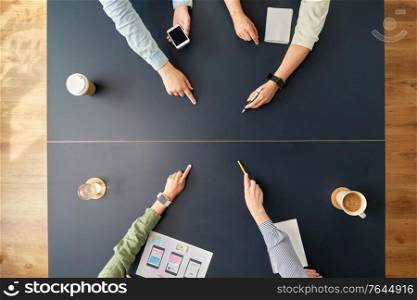 business, people and team work concept - team of startuppers with gadgets and papers pointing fingers to something on office table. business team pointing fingers to office table