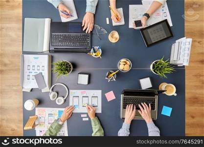 business, people and team work concept - team of startuppers with gadgets and papers working at office table. business team with gadgets working at office table