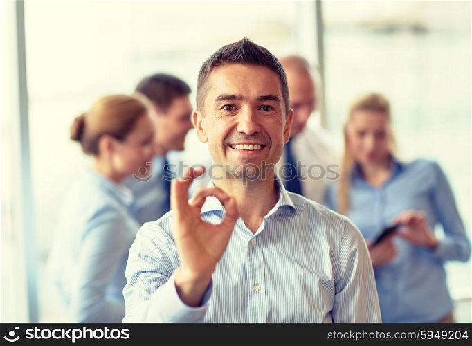 business, people and teamwork concept - smiling businessman showing ok gesture with group of businesspeople meeting in office