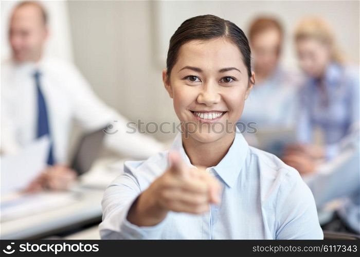 business, people and teamwork concept - smiling businesswoman pointing finger at you with group of businesspeople meeting in office