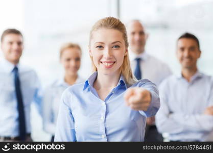 business, people and teamwork concept - smiling businesswoman pointing finger on you with group of businesspeople in office