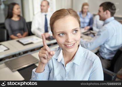 business, people and teamwork concept - smiling businesswoman pointing finger up with group of businesspeople meeting in office