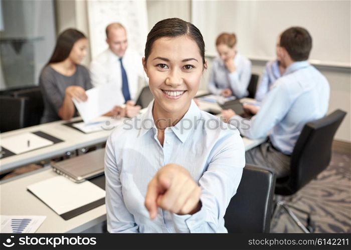 business, people and teamwork concept - smiling businesswoman pointing finger up with group of businesspeople meeting in office