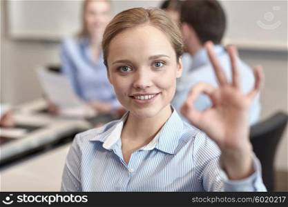 business, people and teamwork concept - smiling businesswoman showing ok gesture with group of businesspeople meeting in office