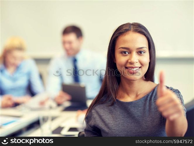 business, people and teamwork concept - smiling businesswoman showing thumbs up with group of businesspeople meeting in office