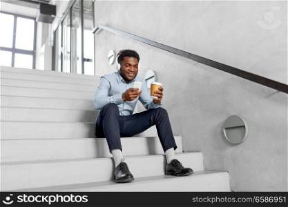 business, people and technology concept - african american businessman with headphones and smartphone listening to music at coffee break on office stairs. businessman in phones with smartphone on stairs