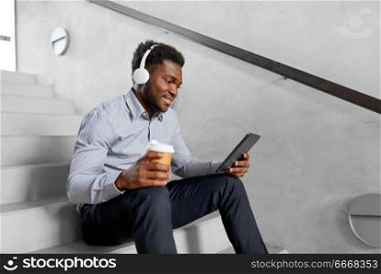business, people and technology concept - african american businessman with headphones and tablet pc computer listening to music at office coffee break. businessman with headphones and tablet pc. businessman with headphones and tablet pc