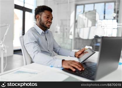 business, people and technology concept - african american businessman with laptop and tablet pc computer at office. businessman with laptop and tablet pc at office. businessman with laptop and tablet pc at office