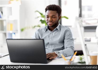 business, people and technology concept - african american businessman with laptop computer working at office. african american businessman with laptop at office. african american businessman with laptop at office