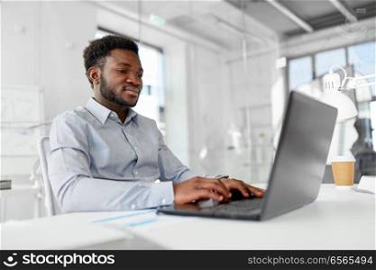 business, people and technology concept - african american businessman with laptop computer working at office. african american businessman with laptop at office