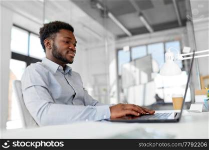 business, people and technology concept - african american businessman with laptop computer working at office. african american businessman with laptop at office