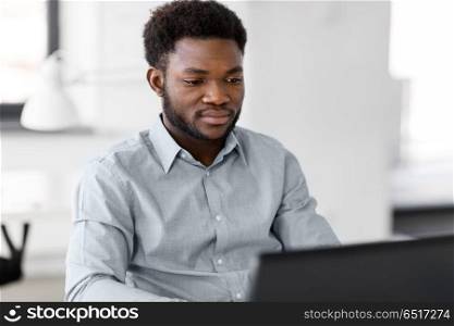 business, people and technology concept - african american businessman with laptop working computer at office. african american businessman with laptop at office. african american businessman with laptop at office