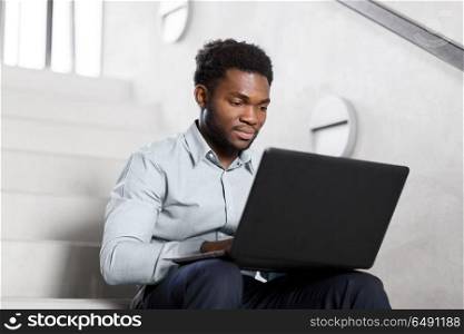 business, people and technology concept - african american businessman with laptop working computer at office stairs. african american businessman with laptop at office. african american businessman with laptop at office