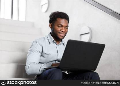business, people and technology concept - african american businessman with laptop working computer at office stairs. african american businessman with laptop at office. african american businessman with laptop at office