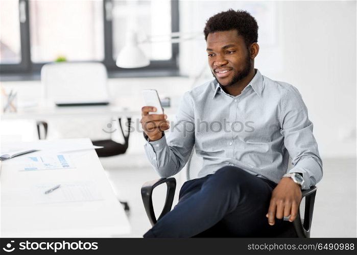 business, people and technology concept - african american businessman with smartphone at office. businessman with smartphone at office. businessman with smartphone at office