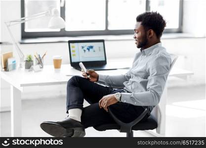 business, people and technology concept - african american businessman with smartphone at office. businessman with smartphone at office. businessman with smartphone at office