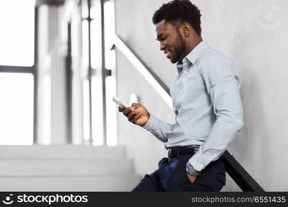 business, people and technology concept - african american businessman with smartphone at office stairs. businessman with smartphone at office stairs. businessman with smartphone at office stairs