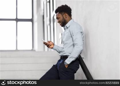 business, people and technology concept - african american businessman with smartphone at office stairs. businessman with smartphone at office stairs. businessman with smartphone at office stairs
