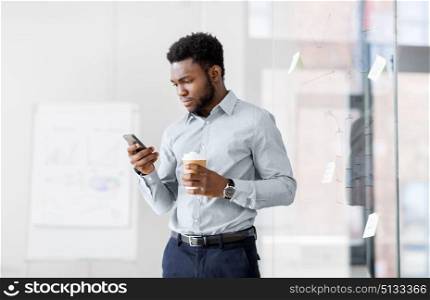 business, people and technology concept - african american businessman with smartphone having break and drinking coffee at office glass board. businessman with smartphone and coffee at office. businessman with smartphone and coffee at office