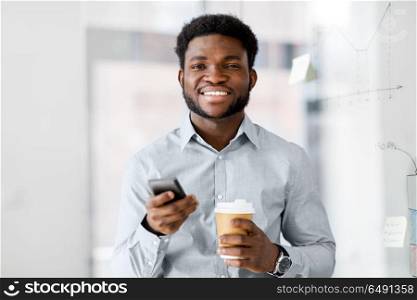 business, people and technology concept - african american businessman with smartphone having break and drinking coffee at office. businessman with smartphone and coffee at office. businessman with smartphone and coffee at office