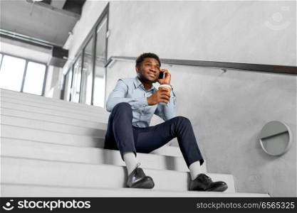 business, people and technology concept - african american businessman with smartphone having break and drinking coffee at office. businessman with smartphone and coffee at office