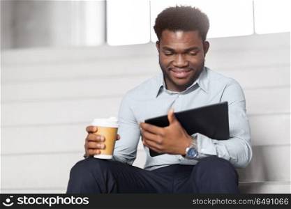 business, people and technology concept - african american businessman with tablet pc computer drinking coffee at office stairs. businessman with tablet pc and coffee on stairs. businessman with tablet pc and coffee on stairs