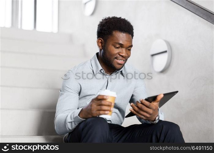 business, people and technology concept - african american businessman with tablet pc computer drinking coffee at office stairs. businessman with tablet pc and coffee on stairs. businessman with tablet pc and coffee on stairs