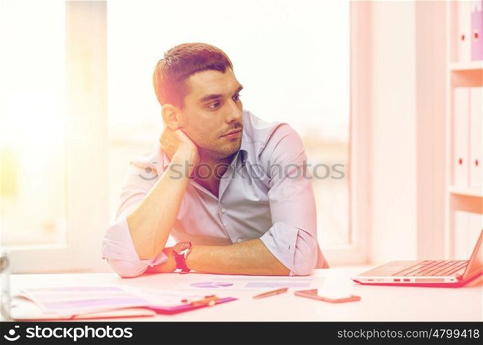 business, people and technology concept - bored businessman with laptop computer and papers at office