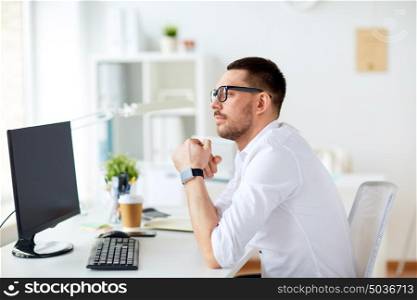 business, people and technology concept - businessman in glasses sitting at office computer and thinking. businessman in glasses sitting at office computer