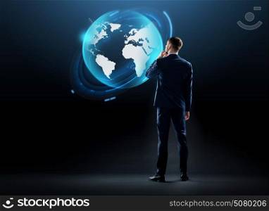 business, people and technology concept - businessman in suit looking at earth globe hologram over black background. businessman looking at earth globe hologram
