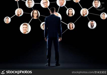 business, people and technology concept - businessman in suit with virtual icons of corporate network over black background. businessman with virtual corporate network