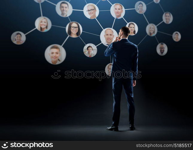 business, people and technology concept - businessman in suit with virtual icons of corporate network over black background. businessman with virtual corporate network