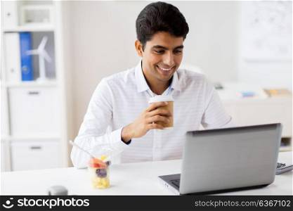 business, people and technology concept - businessman with laptop computer having meal break and drinking coffee at office. businessman with laptop drinking coffee at office